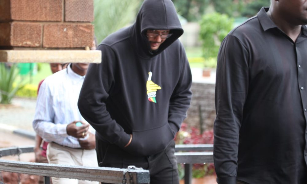 Adam Markov, wearing a hoodie, arrives at a Zimbabwean court under police custody following his arrest on charges of vehicle theft and fraudulent activities.