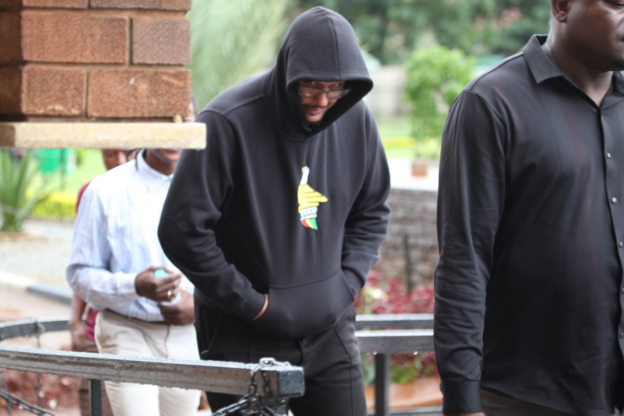 Adam Markov, wearing a hoodie, arrives at a Zimbabwean court under police custody following his arrest on charges of vehicle theft and fraudulent activities.